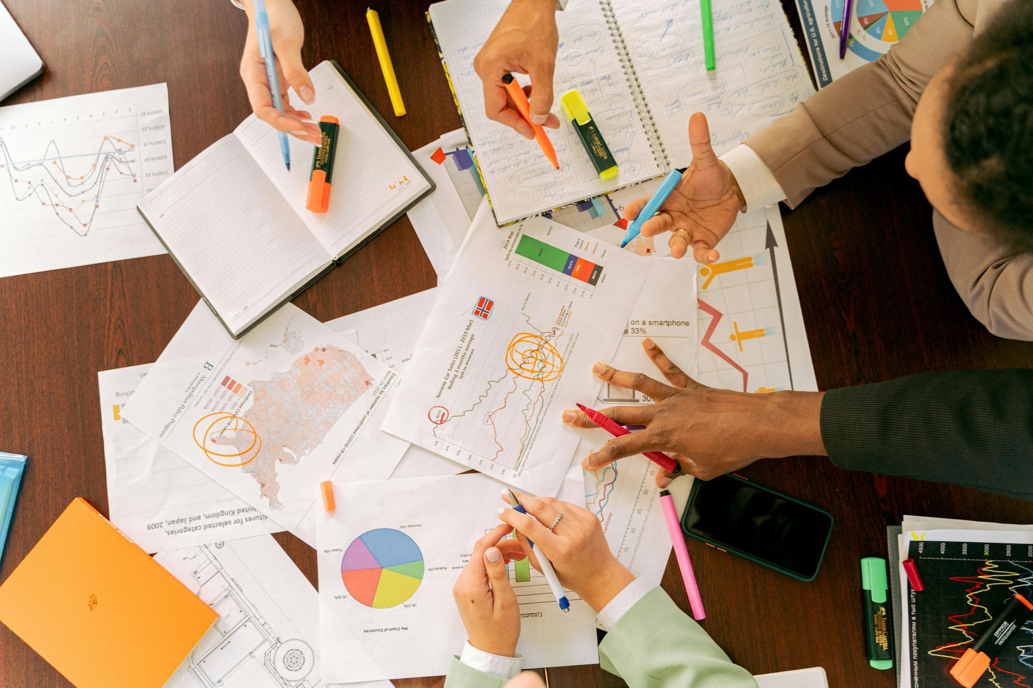 A magnifying glass, pencils and printed business reports laid on a wooden table.