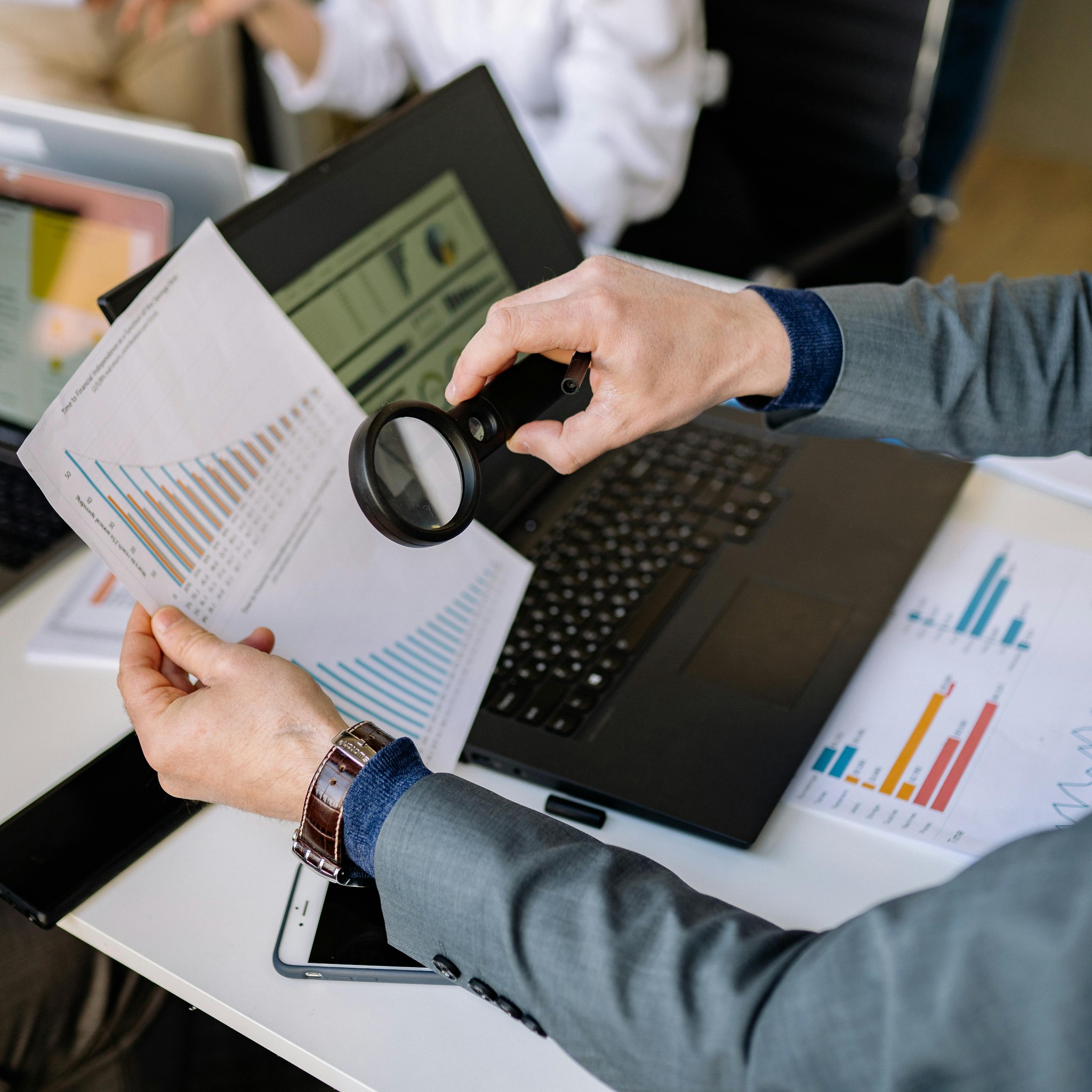 A magnifying glass placed over a financial chart on a desk beside a laptop and stationery.